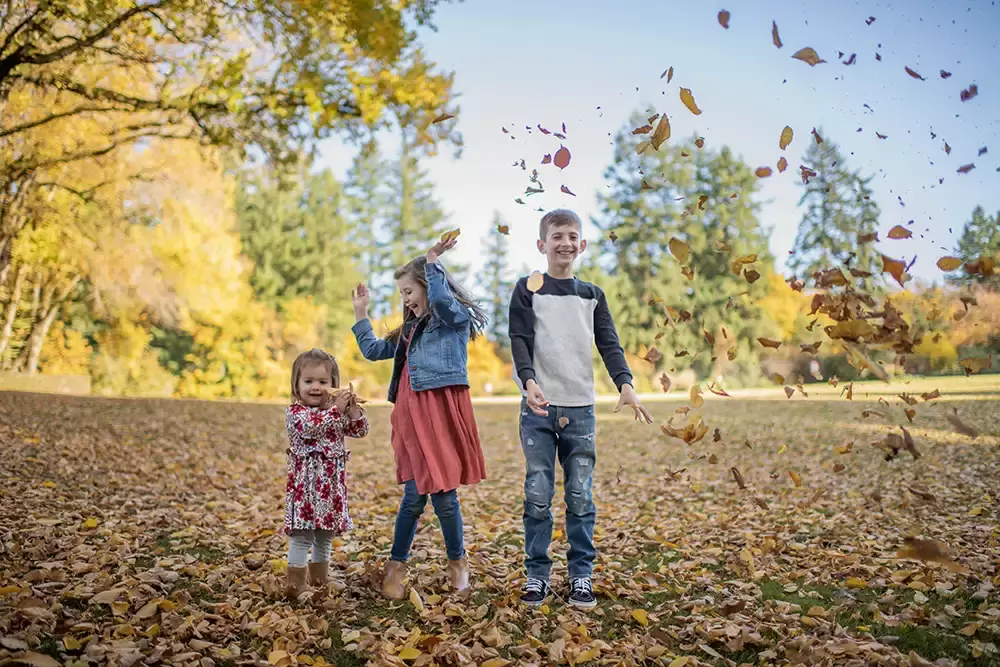 Family Photographer Portland Oregon Robert Knapp catches three children throwing leafs in the air and smiling for their portrait. 