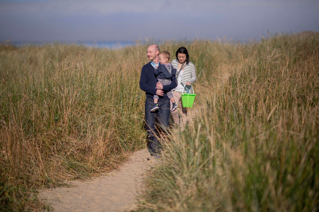 A family walks on a sandy path in the dune grasses near the sea together
