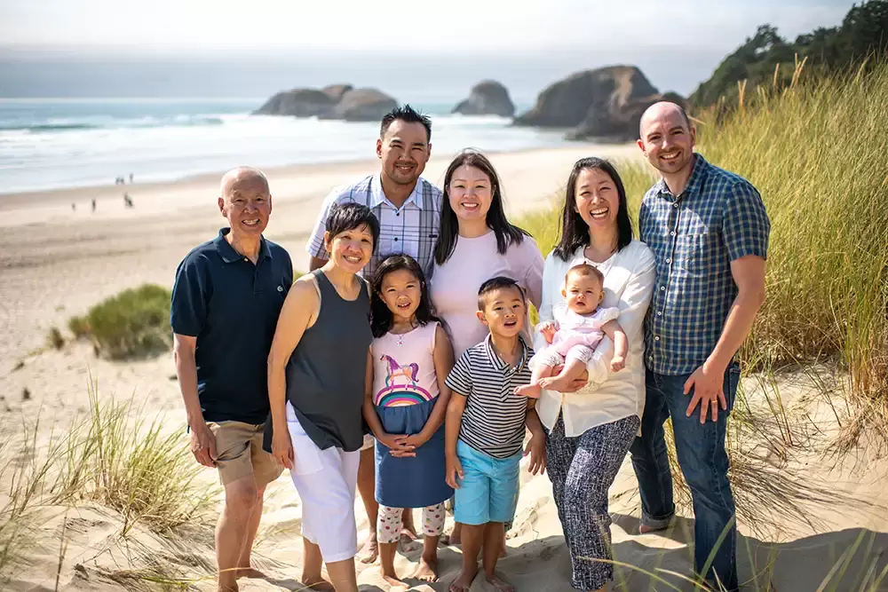 a family stands in the sand and looks to the camera , the ocean and waves are behind them Portland ​Family Photographer Robert Knapp - Book Today!