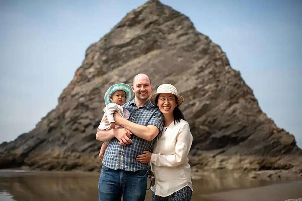 a family stands in front of a giant rock rising from the ocean Portland ​Family Photographer Robert Knapp - Book Today!