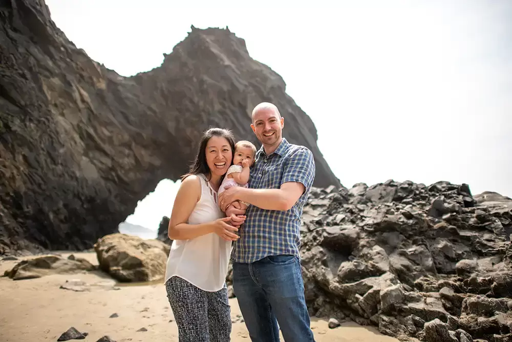 mom dad and baby stand by the ocean and smile to the camera Portland ​Family Photographer Robert Knapp - Book Today!