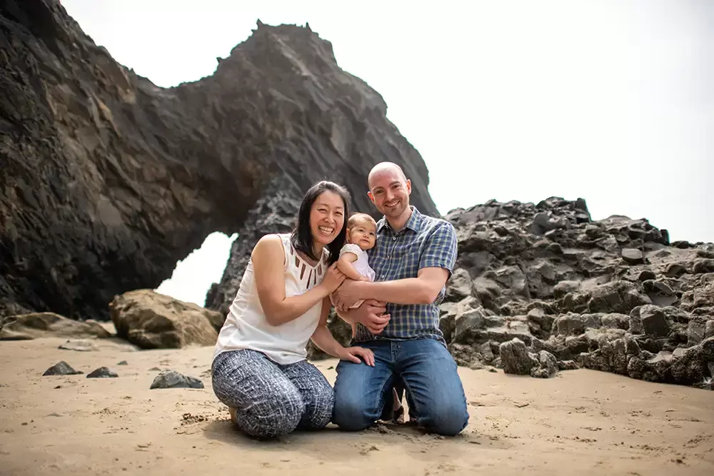 a family of three on the beach near the rocks smile at the camera Portland ​Family Photographer Robert Knapp - Book Today!