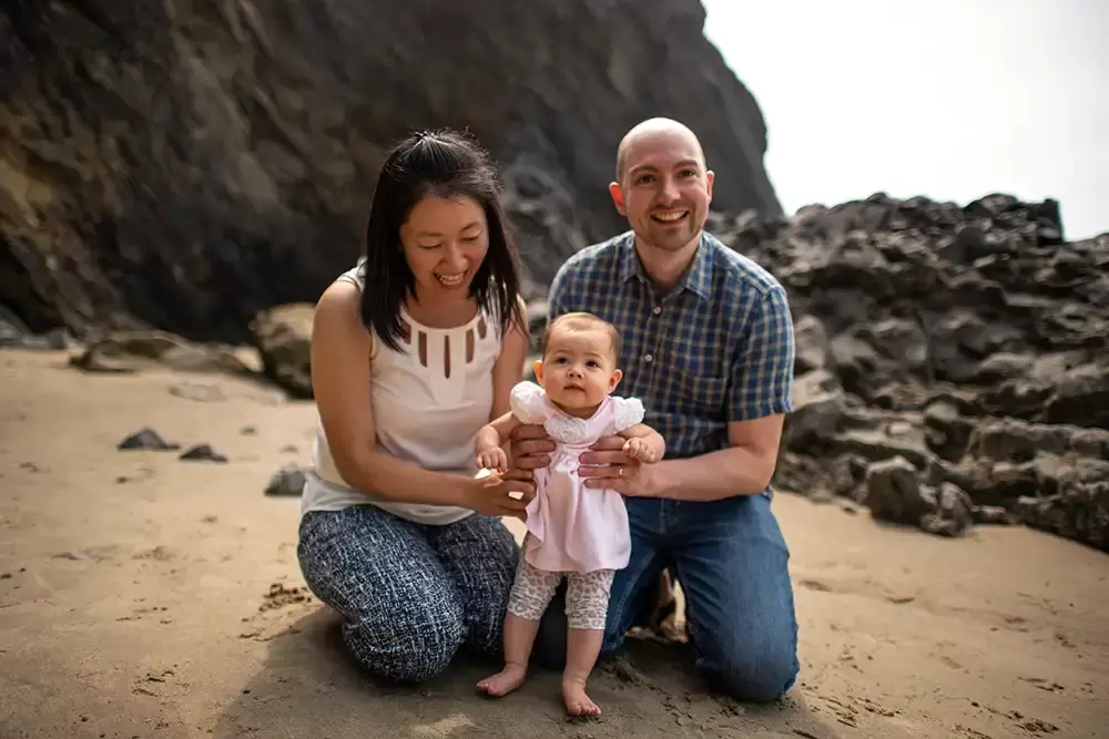 father and mother hold up baby in the sand. She is not ready to walk yet Portland ​Family Photographer Robert Knapp - Book Today!​Family Photographer Robert Knapp in Portland - Book Today!