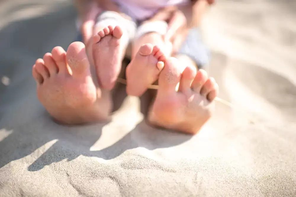 A close-up photo of baby feet and mamas feet on the sand at the beach Portland ​Family Photographer Robert Knapp - Book Today! ​Family Photographer Robert Knapp in Portland - Book Today!