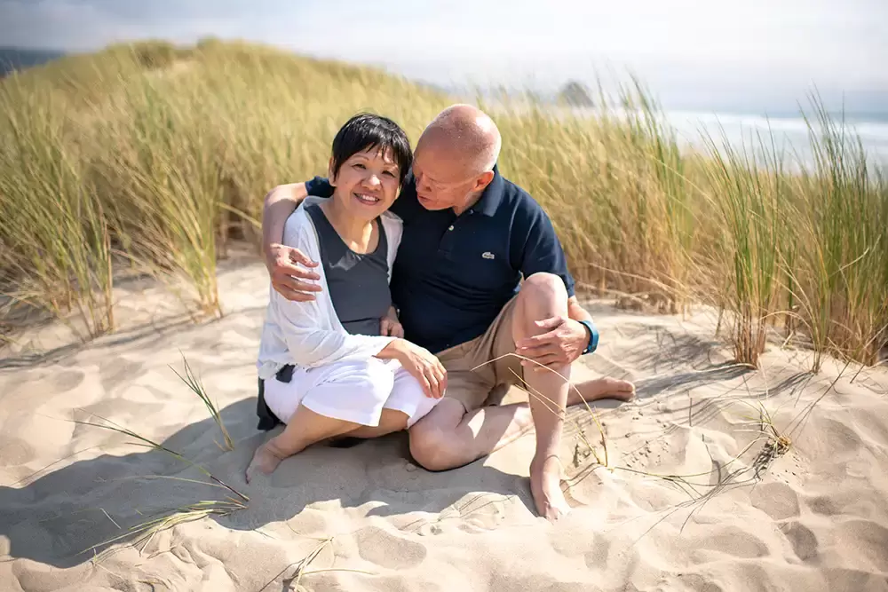 Grandma and grandpa sit in the sand on the beach. The ocean is in the distance. Portland ​Family Photographer Robert Knapp - Book Today! ​Family Photographer Robert Knapp in Portland - Book Today!