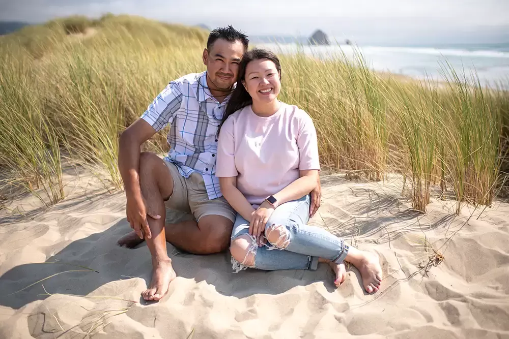 A couple sit on the beach and smiles to the camera with the ocean in the distance Portland ​Family Photographer Robert Knapp - Book Today! ​Family Photographer Robert Knapp in Portland - Book Today!