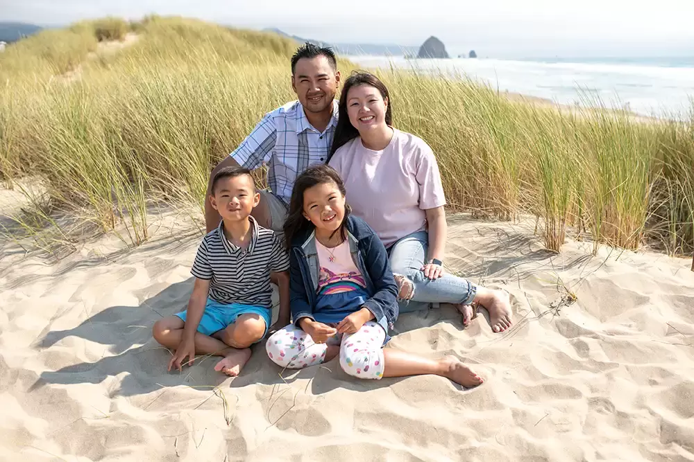 Family of four sit on the beach in the sun and smiles at the camera Portland ​Family Photographer Robert Knapp - Book Today!​Family Photographer Robert Knapp in Portland - Book Today!