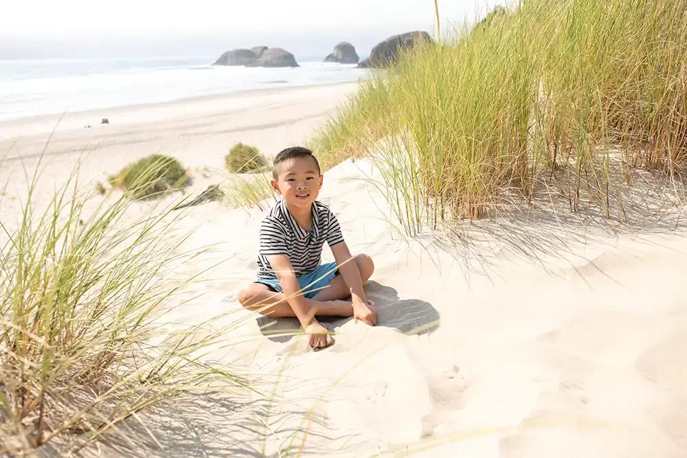 A little boy climbs a Sandune and sits at the top and smiles Portland ​Family Photographer Robert Knapp - Book Today! ​Family Photographer Robert Knapp in Portland - Book Today!