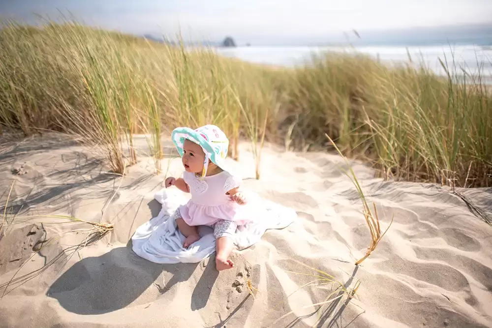 a baby sits in the sand with the ocean in the distance Portland ​Family Photographer Robert Knapp - Book Today! ​Family Photographer Robert Knapp in Portland - Book Today!