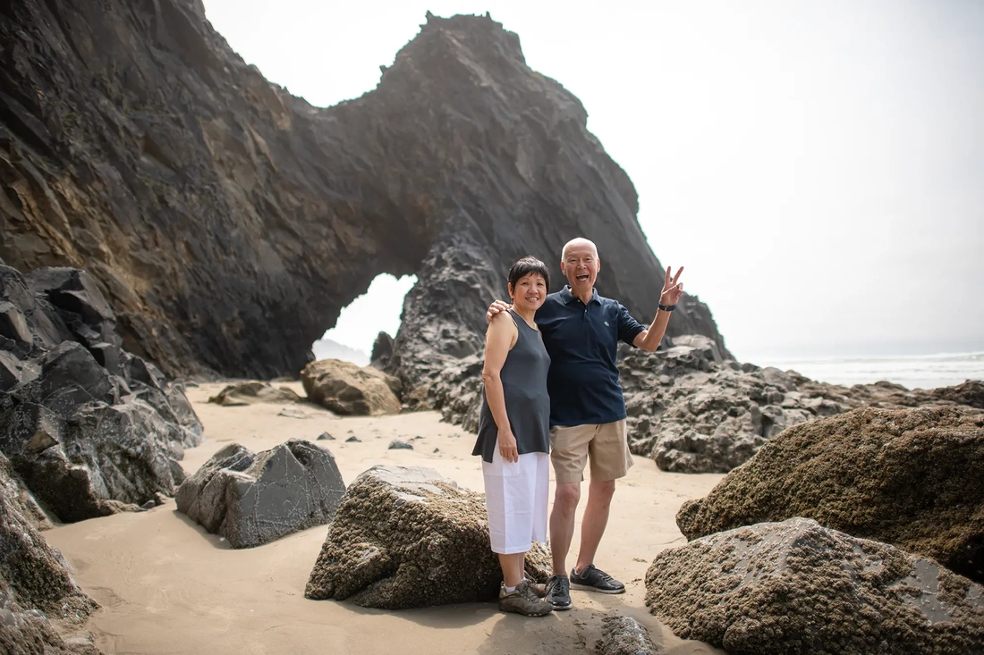 grandparents stand in front of a stone arch at the beach with big smiles Portland ​Family Photographer Robert Knapp - Book Today!