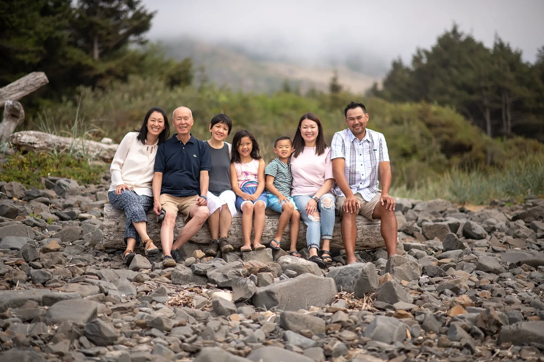 a family sits on a driftwood log together and smiles to the camera Portland ​Family Photographer Robert Knapp - Book Today!