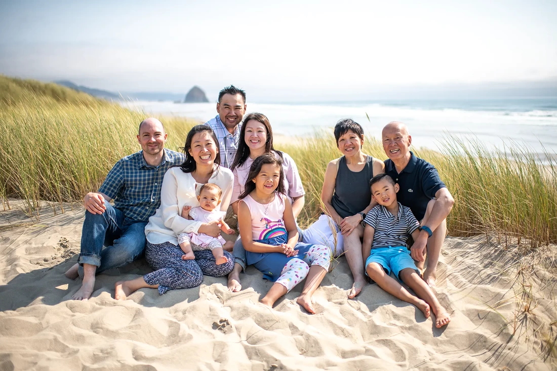 a family sits in the sand with the ocean and some sea grasses behind them Portland ​Family Photographer Robert Knapp - Book Today!