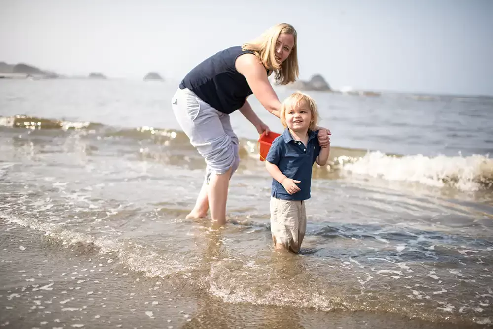 pictures of families on the beach the waves begin to get ankle deep on the mother and knees deep on the little boy. together they smile on at the beech.   Family Pictures Beach Theme with Portland Family Photographer Robert Knapp