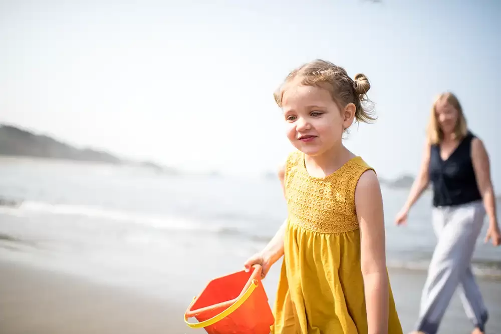 ideas for family beach pictures a little girl holds a bucket for making a sand castle on the beach, mother walks behind in the sand   Family Pictures Beach Theme with Portland Family Photographer Robert Knapp