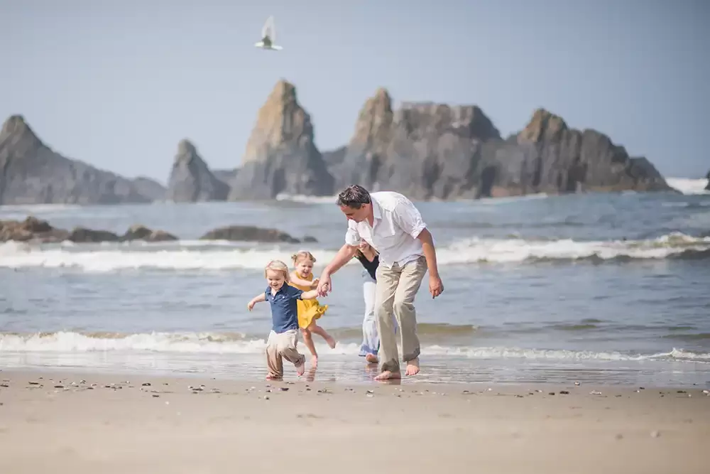 fun photos on the beach of running with a dramatic background of a jagged rocky coastline   Family Pictures Beach Theme with Portland Family Photographer Robert Knapp