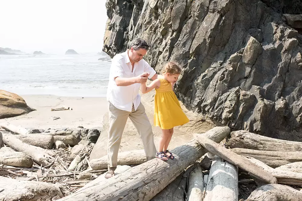 father and daughter climb over driftwood logs   Family Pictures Beach Theme with Portland Family Photographer Robert Knapp