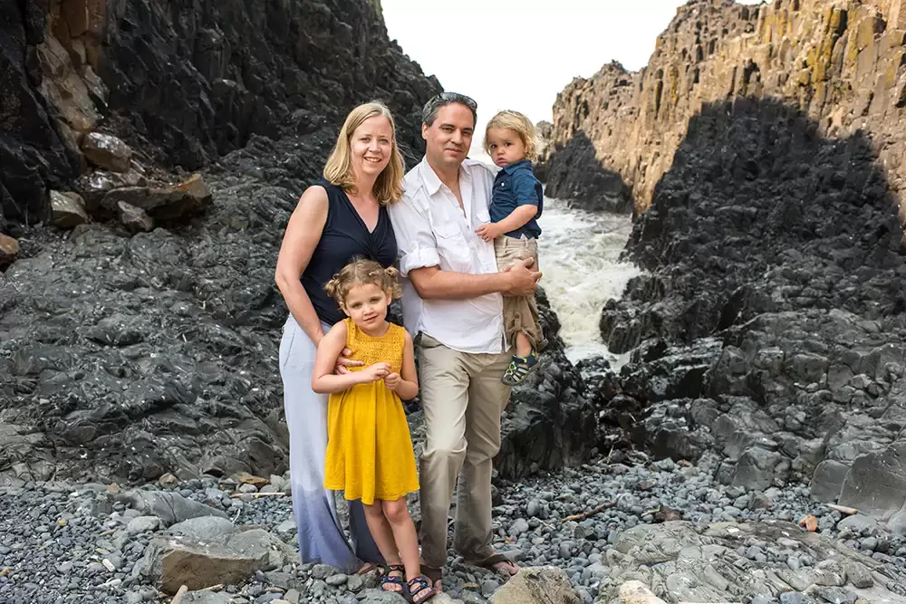 a family poses in front of a narrow cove with waves splashing up   Family Pictures Beach Theme with Portland Family Photographer Robert Knapp