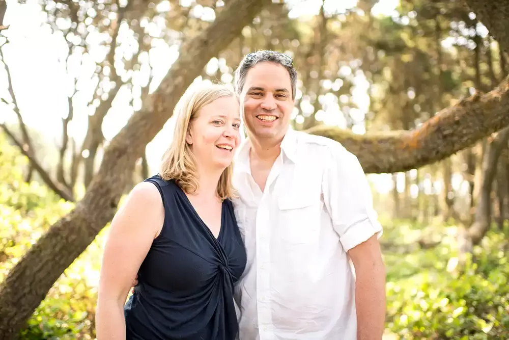 man and wife look to the camera with a smile with tree branches out of focus in the distance   Family Pictures Beach Theme with Portland Family Photographer Robert Knapp