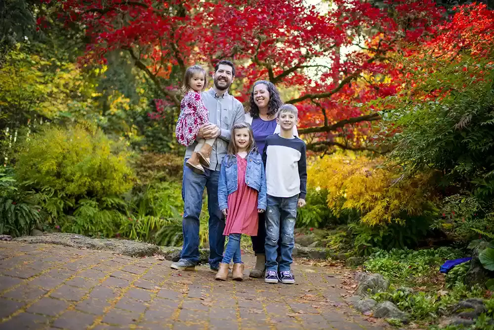 Portland Family Photographer Robert Knapp captures a family standing in front of a brightly colored tree. Autum foliage of light green and yellow around, the tree in back of the family is bright red. All are happy and focused