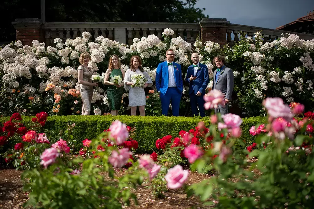 Polaris Hall
Portland Oregon Wedding Venue
Photographer Robert Knapp at Modern Art Photograph the wedding party stands in the rose garden. Roses are almost everywhere in the photo. 
