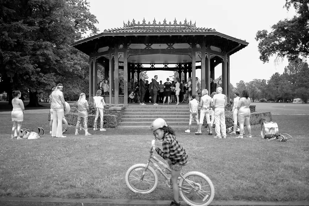 Polaris Hall
Portland Oregon Wedding Venue
Photographer Robert Knapp at Modern Art Photograph wedding ceremony under the gazebo in the foreground a child from the neighborhood on a bicycle is curious and stops to see what is going on near the gazebo. A brass band waits for the ceremony to be done under the gazebo, the bride and groom face each other all the wedding guests are surrounding.