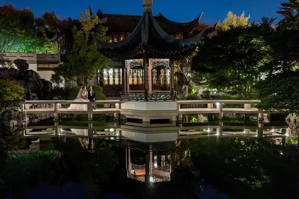 Portland Wedding Photographers at Modern Art Photograph The Photojournalist Wedding Photography of Robert Knapp at the Chinese garden working after dark with no flash. bride and groom sit on the bench leading to the pagoda, their reflection is in the water. 