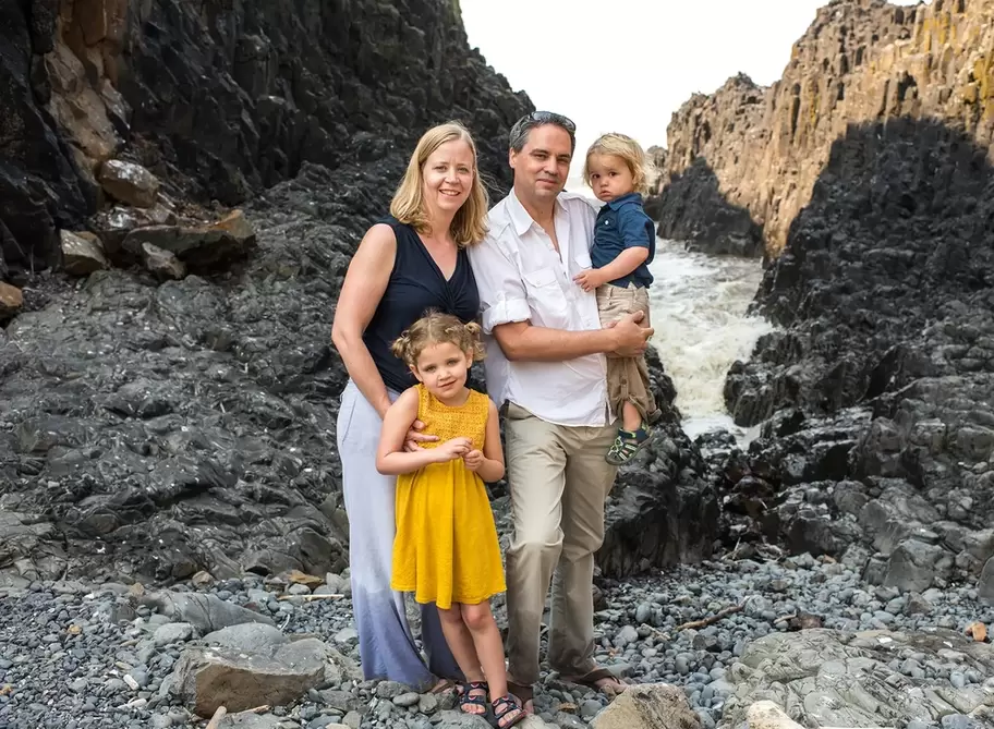   A family stands in front of a rocky cove with waves crashing deep inside. Family Pictures Beach Theme with Portland Family Photographer Robert Knapp