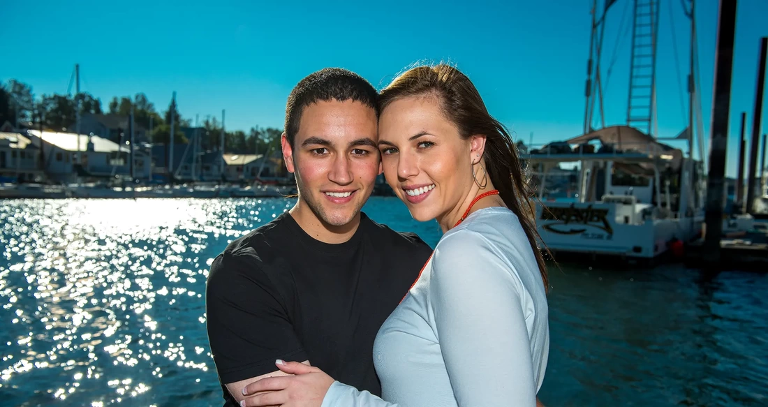 A couple stands at the marina for an engagement photo. 