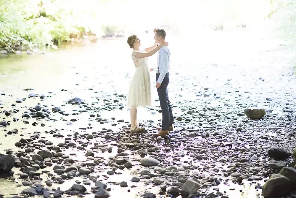 Silver Falls Weddings with Modern Art Photograph bride and groom stand on the stones on the bank of a small river at Silver Falls Weddings with Modern Art Photograph