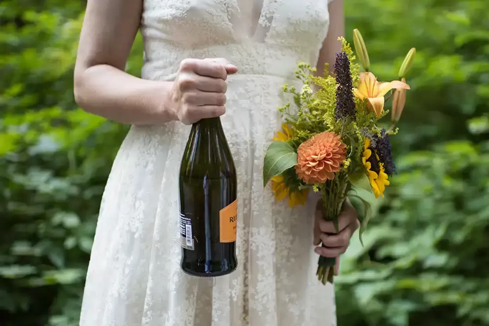 bride clutches her bouquet and a bottle of sparkling wine before the ceremony at Silver Falls Weddings with Modern Art Photograph