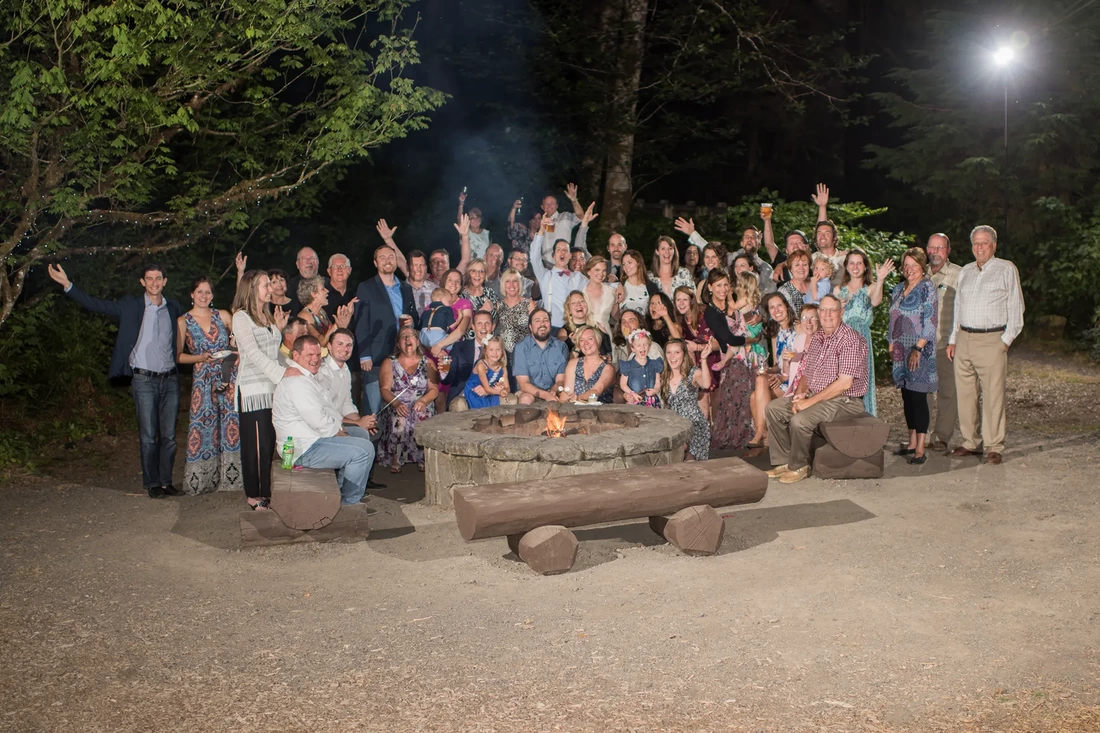 Silver falls weddings offer great backgrounds for family photos during the reception. Pictured here the entire wedding party and both families gather around the fire for a great group photo of the entire party. 