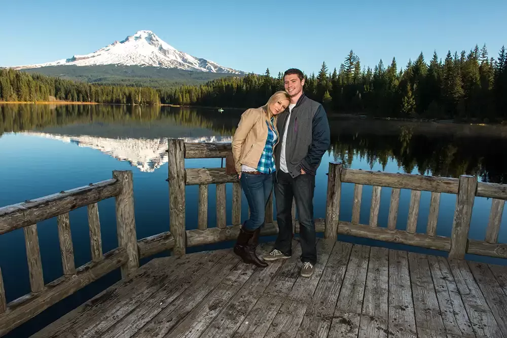 standing on a dock with a railing a couple is in n front of a massive snow capped mountain and untouched forest Unforgettable Moment - Mountain Engagement Photos 
with
​ Photojournalist Photographer Robert Knapp