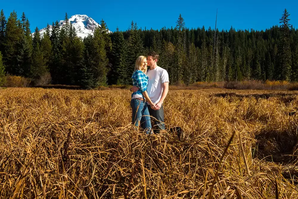 a couple stands in a meadow with a snow capped mountain in the distance Unforgettable Moment - Mountain Engagement Photos 
with
​ Photojournalist Photographer Robert Knapp