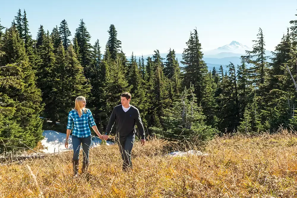 mountain engagement photos of a couple walking through a field with some snow in the shadows Mount Jefferson is in the distance over the horizon. Unforgettable Moment - Mountain Engagement Photos 
with
​ Photojournalist Photographer Robert Knapp
