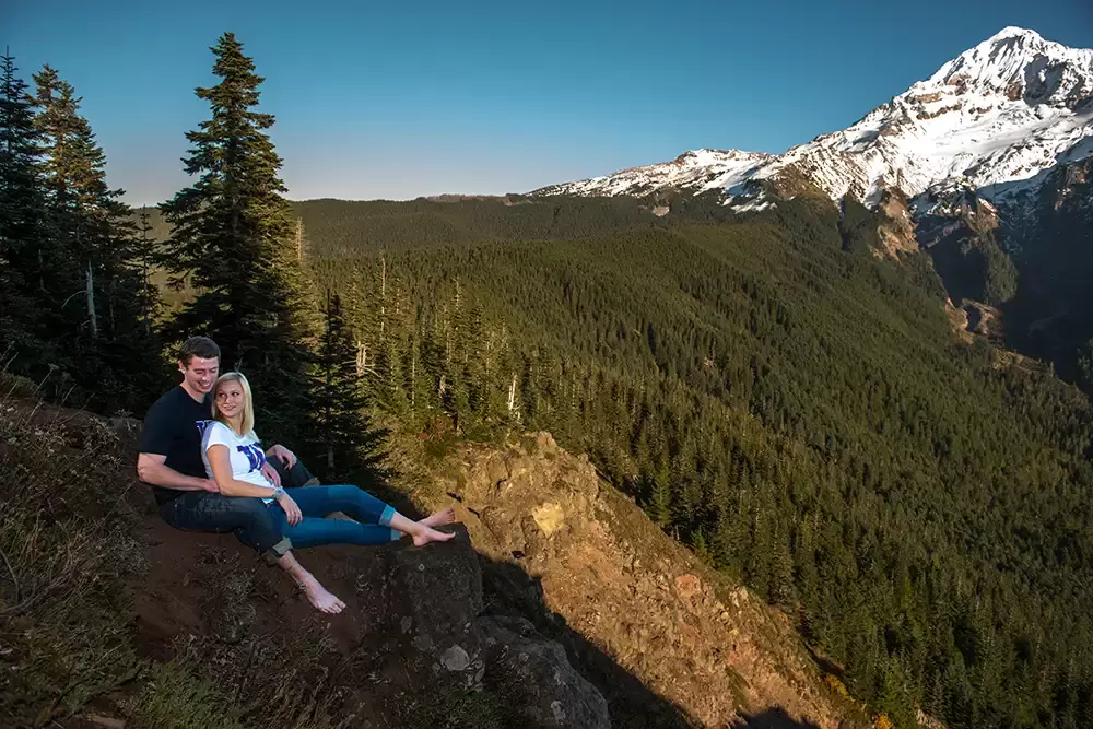 mountain engagement photos of a couple sitting on a rock at the top of a cliff face over a ledge. Mount Hood is in the distance. Unforgettable Moment - Mountain Engagement Photos 
with
​ Photojournalist Photographer Robert Knapp