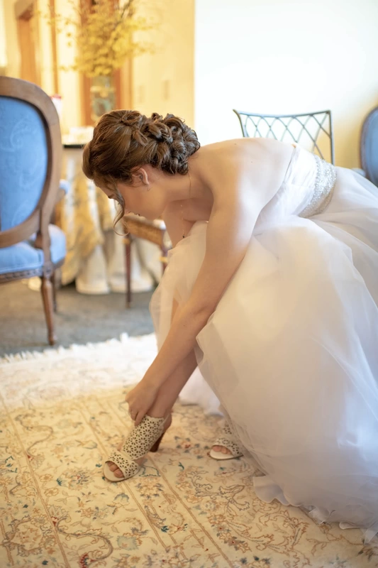 ​Vineyard Wedding Oregon where a bride in a wedding dress leans to strap her shoes