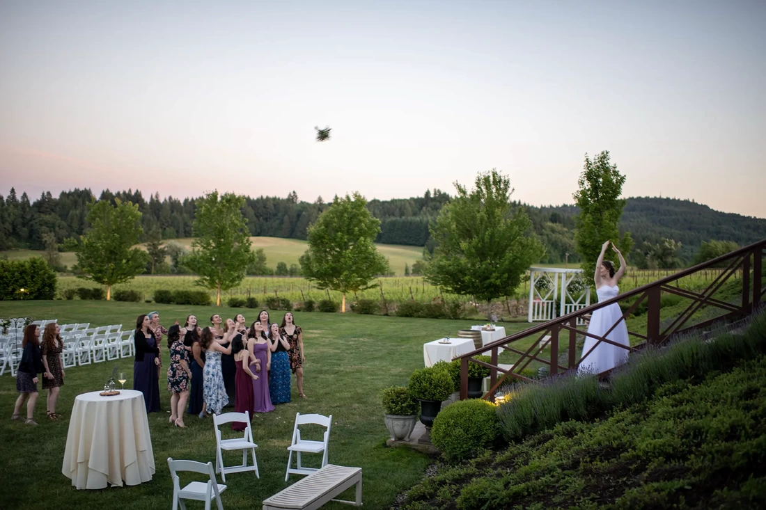 Vineyard Wedding Oregon with the bride tossing her bouquet overhead where it hangs over a small crowd of girls waiting to catch it. 