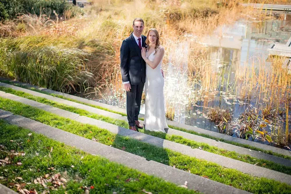 Wedding Photographers in Portland  at the EcoTrust Robert Knapp Photographer A city park water feature containing wild grasses. the bride and groom stand in a beam of light reflected from a tall building. the lighting effect is ineresting