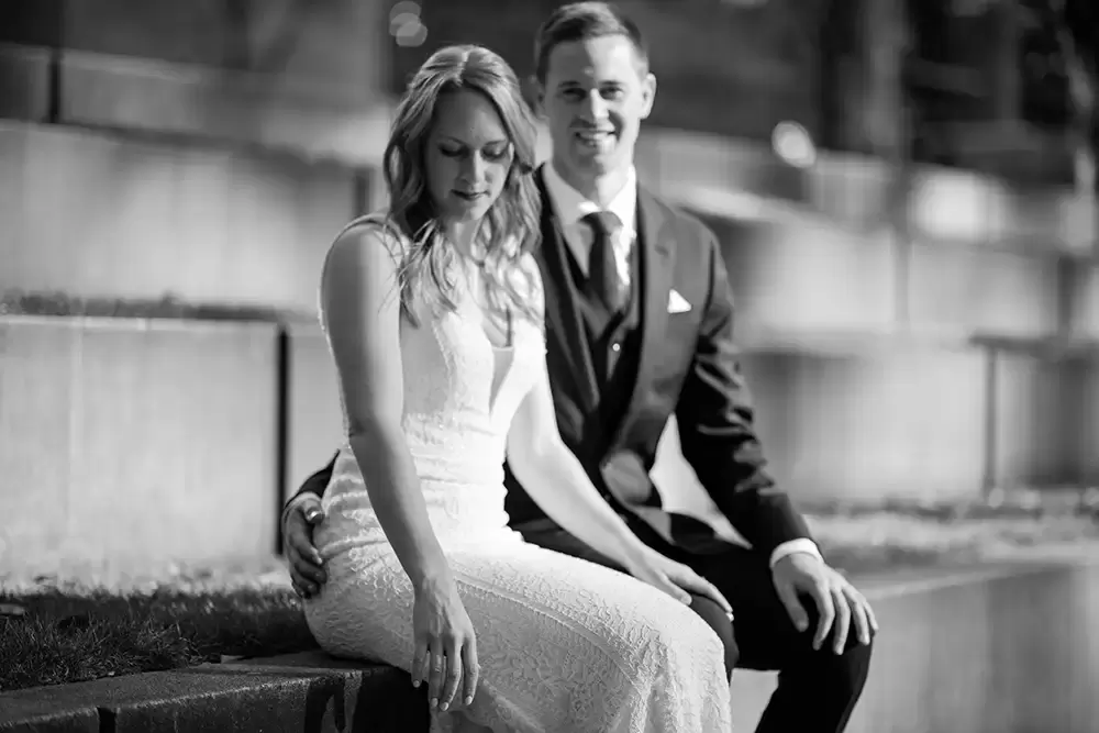 bride and groom sit in the park. the bride is concentrating on something, the groom is focused and smiling. 