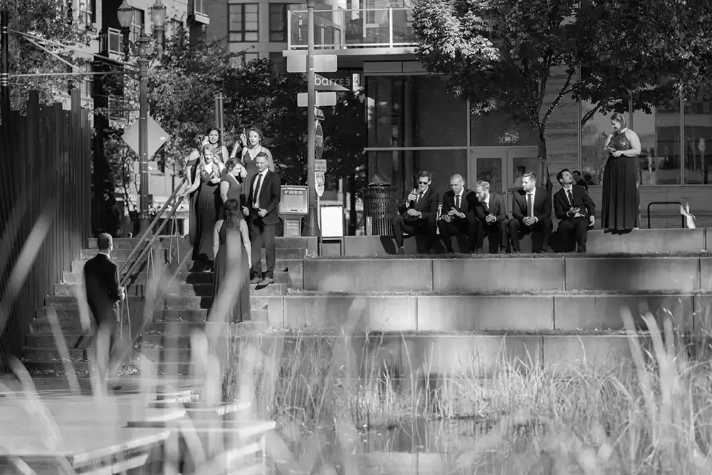 Wedding Photographers in Portland  at the EcoTrust Robert Knapp Photographer the wedding party gathers on the steps in the park. they are all doing their own thing.