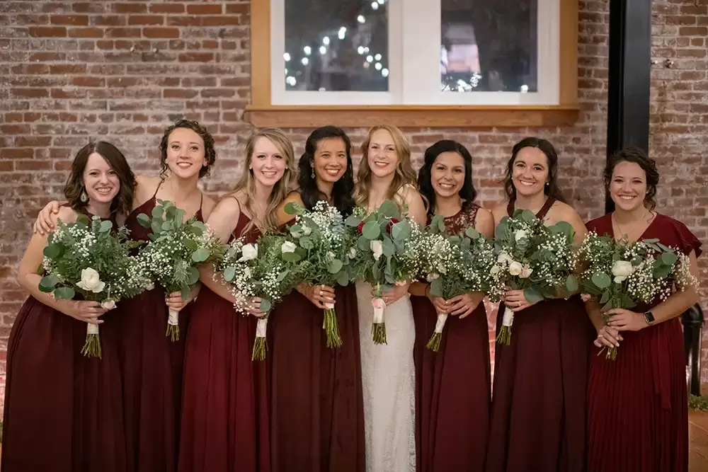 bride with her bridesmaids during the reception. all have their arms around each other and bouquets in hand