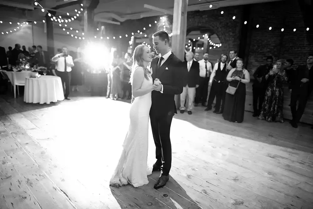 Wedding Photographers in Portland  at the EcoTrust Robert Knapp Photographer First dance full length showing the dress and suit, the string lights criss cross the room. 
