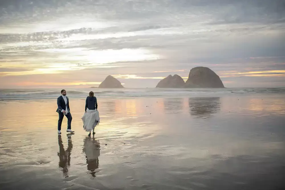 bride and groom walk on the beach at sunset