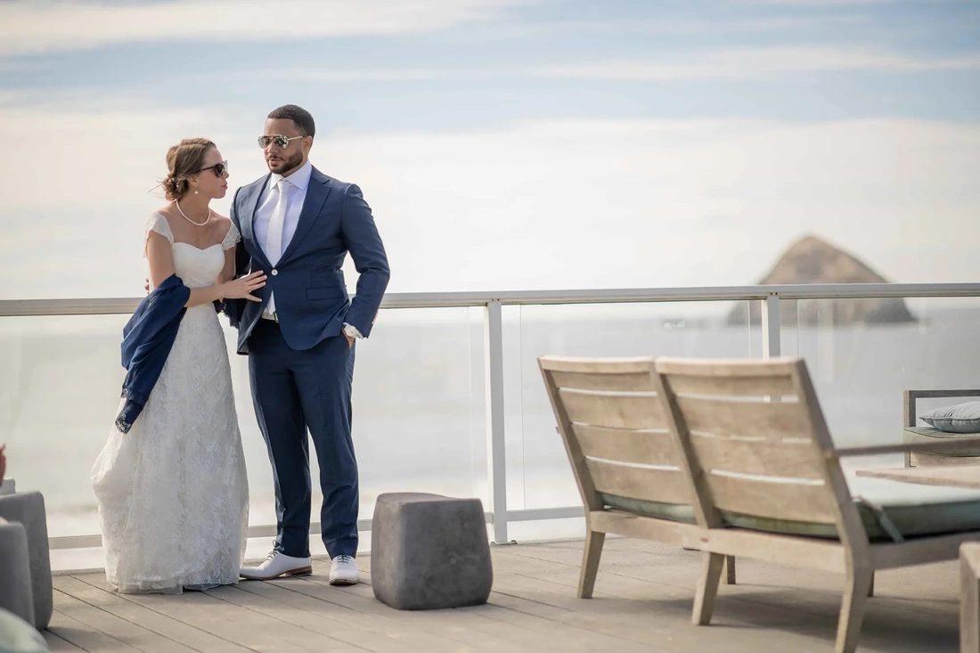 Wedding Photographers Near Me | Modern Art Photograph Wedding Photography from Oceanside, Oregonbride and groom talk on a porch overlooking the ocean with sungalsses on 