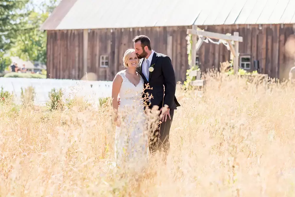 Tin Roof Weddings Barn Weddings Venues Near Me from Photographer Robert Knapp bride and groom are standing in the tall grass the groom kisses the bride on the temple