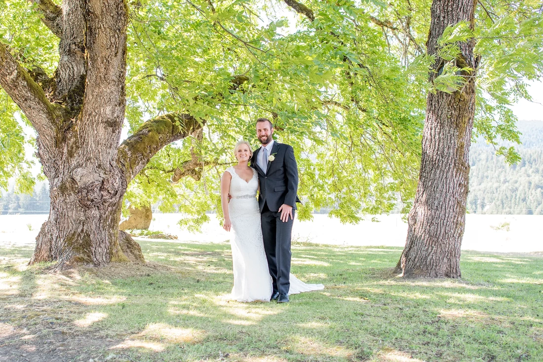 Tin Roof Weddings Barn Weddings Venues Near Me from Photographer Robert Knapp Bride and groom stand between two very large trees. There is a lot of bright white light. Tin Roof Weddings Barn Weddings Venues Near Me